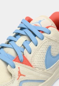 Zatvoreni prikaz bež i koraljnih tenisica sa svijetloplavim vezicama, mrežastim panelima i plavim Nike swoosh logotipom.