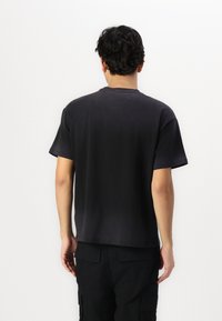 Black cotton T-shirt with short sleeves, a crew neck, and a relaxed fit. The back features a smooth texture with no visible embellishments.
