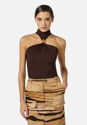 Donna con i capelli tirati indietro indossa un top nero senza maniche con collo all'americana e una gonna beige con motivi a strisce nere che ricordano il tigre e tasche.