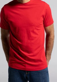 T-shirt en coton rouge avec col rond et manches courtes ; texture lisse ; portée avec un jean bleu. Design simple et uni sans motifs.