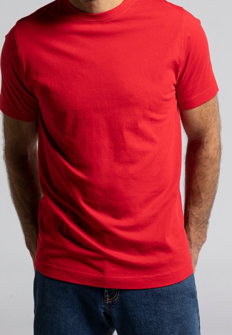 T-shirt en coton rouge avec col rond et manches courtes ; texture lisse ; portée avec un jean bleu. Design simple et uni sans motifs.