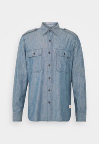 Zasněžovaná světle modrá riflová košile s dlouhým rukávem, knoflíkovým zapínáním vpředu, dvěma náprsními kapsami s klopami a epolety na ramenou.