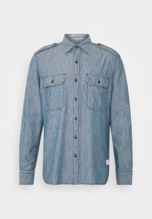 Camisa de denim de manga larga en un tono azul claro, con botones en la parte delantera, dos bolsillos en el pecho con solapas y hombreras.