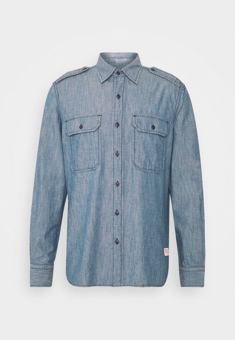 Zasněžovaná světle modrá riflová košile s dlouhým rukávem, knoflíkovým zapínáním vpředu, dvěma náprsními kapsami s klopami a epolety na ramenou.