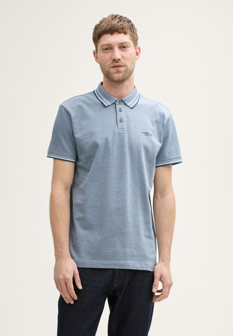 Polo shirt in lichtblauw met een twee-knopen knoopsluiting, contrasterende kraag en mouwstreepjes, en een subtiele logo-details op de borst.