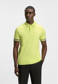 Kortärmad pikétröja i klar gul, med krage och svarta ränder på ärmsluten. Slät textur, figursydd design och enkel stil.