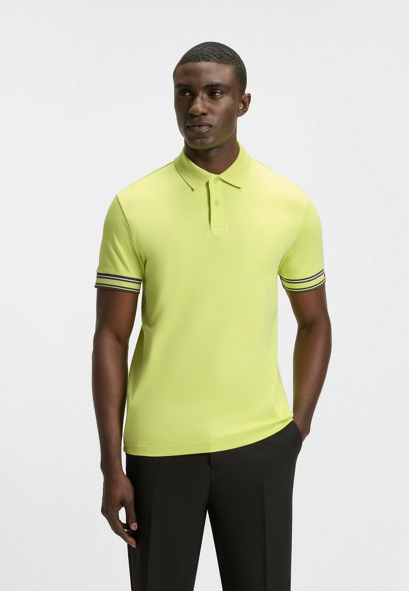 Kortärmad pikétröja i klar gul, med krage och svarta ränder på ärmsluten. Slät textur, figursydd design och enkel stil.