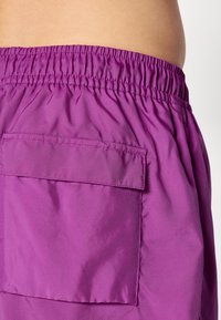 Lilla shorts med elastisk midjebånd og en baklomme. Stoffet virker lett og glatt med en subtil glans.