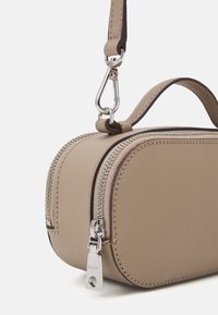 Béžová obdélníková taška vyrobená z texturovaného materiálu, se stříbrným zipem a odnímatelným popruhem s kovovým klipem. Hladké akcenty po celém povrchu.