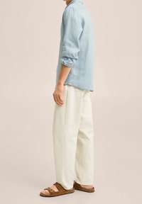 Jasnoniebieska koszula z długim rękawem, białe spodnie o luźnym kroju i brązowe sandały. Koszula ma podwinięte rękawy; gładka tekstura z kołnierzykiem.