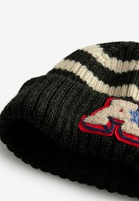 Schwarze Strickmütze mit beigen Streifen, die eine gerippte Textur aufweist und ein auffälliges Patch in Rot und Creme mit blauen Akzenten hat.