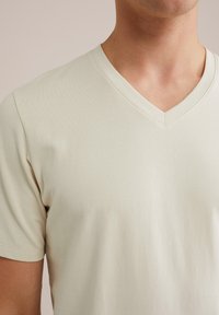 Světlý béžový tričko s V výstřihem vyrobené z měkké bavlněné směsi. Krátké rukávy a hladký povrch, vhodné pro volný čas.