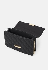 Sac en cuir noir matelassé avec fermoir en or et chaîne, rabat ouvert révélant des compartiments intérieurs, sur fond blanc.