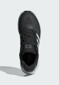 Zapatilla deportiva negra con acentos grises, parte superior texturizada, cordones gruesos y tres franjas blancas. Cuenta con una suela acolchada y punta redondeada.