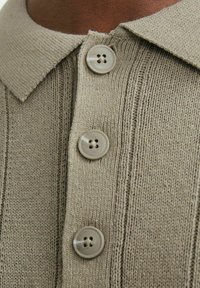 Knit-paita beige väri, jossa on kauluspanssari, neljä nappia ja pystyribattua tekstiiliä.