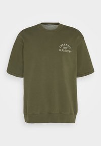 Sudadera oversized de color verde oliva con mangas cortas, cuello y dobladillo acanalados, que presenta el texto en blanco "Carhartt WIP Class of 89" en el frente.