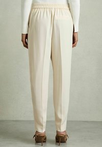 Pantaloni color crema con vita elastica, pieghe, tasche laterali e un design elegante. Indossato con sandali con tacco a strati marroni.