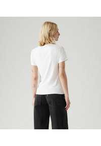 Camiseta de algodón blanca con mangas cortas, de corte ajustado y cuello de canalé. Combinada con jeans oscuros de tiro alto.
