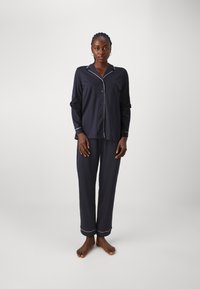 Marinblå pyjamasset gjort av mjukt tyg, med en skjorta med knappar och vit piping samt matchande byxor med fållaccenter.