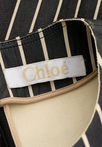 Tissu rayé noir et beige avec une étiquette blanche cousue à l'intérieur portant la mention « Chloé » en broderie beige.