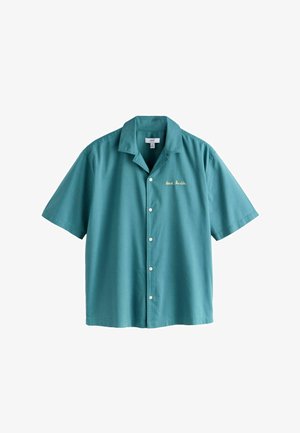 Žalsvai mėlyna trumpomis rankovėmis marškiniai su kampine apykakle ir mažomis baltomis siuvinėtomis raidėmis kairėje krūtinės pusėje, kuriose parašyta „Henri Matin“.