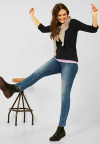 Zwarte longsleeve top gecombineerd met een lichtroze shirt, blauwe skinny jeans en zwarte enkellaarzen met gestructureerde zolen. Een beige sjaal hangt erover.