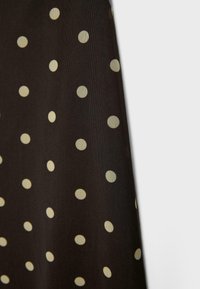 Černá látka s rovnoměrně rozmístěnými bílými puntíky, zobrazující texturu a mírné záhyby na jednoduchém světlém pozadí.