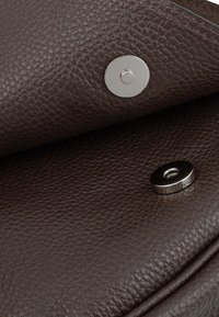 Brown textured leather with visible grain, featuring two metal snap closures. The design includes a smooth, polished accent.