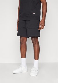 Shorts noirs en coton avec deux poches avant, assortis à des baskets blanches et des chaussettes arrivant à la cheville. Stylé avec un sweat à capuche sombre assorti.