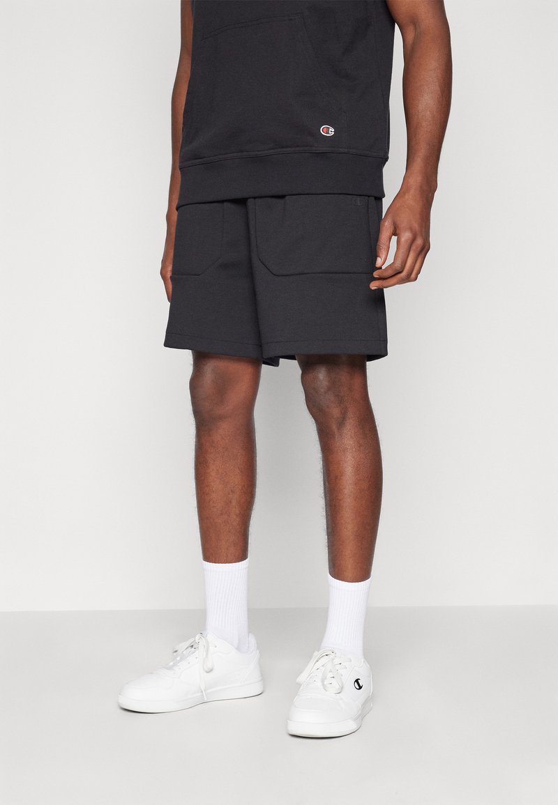 Shorts noirs en coton avec deux poches avant, assortis à des baskets blanches et des chaussettes arrivant à la cheville. Stylé avec un sweat à capuche sombre assorti.