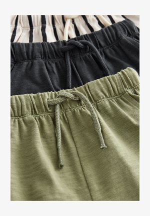 Tri páry šortiek ležia rovno: jedna béžová s čiernymi pruhmi, jedna úplne čierna a jedna zelená. Všetky majú elastické pásy a sťahovacie šnúrky.