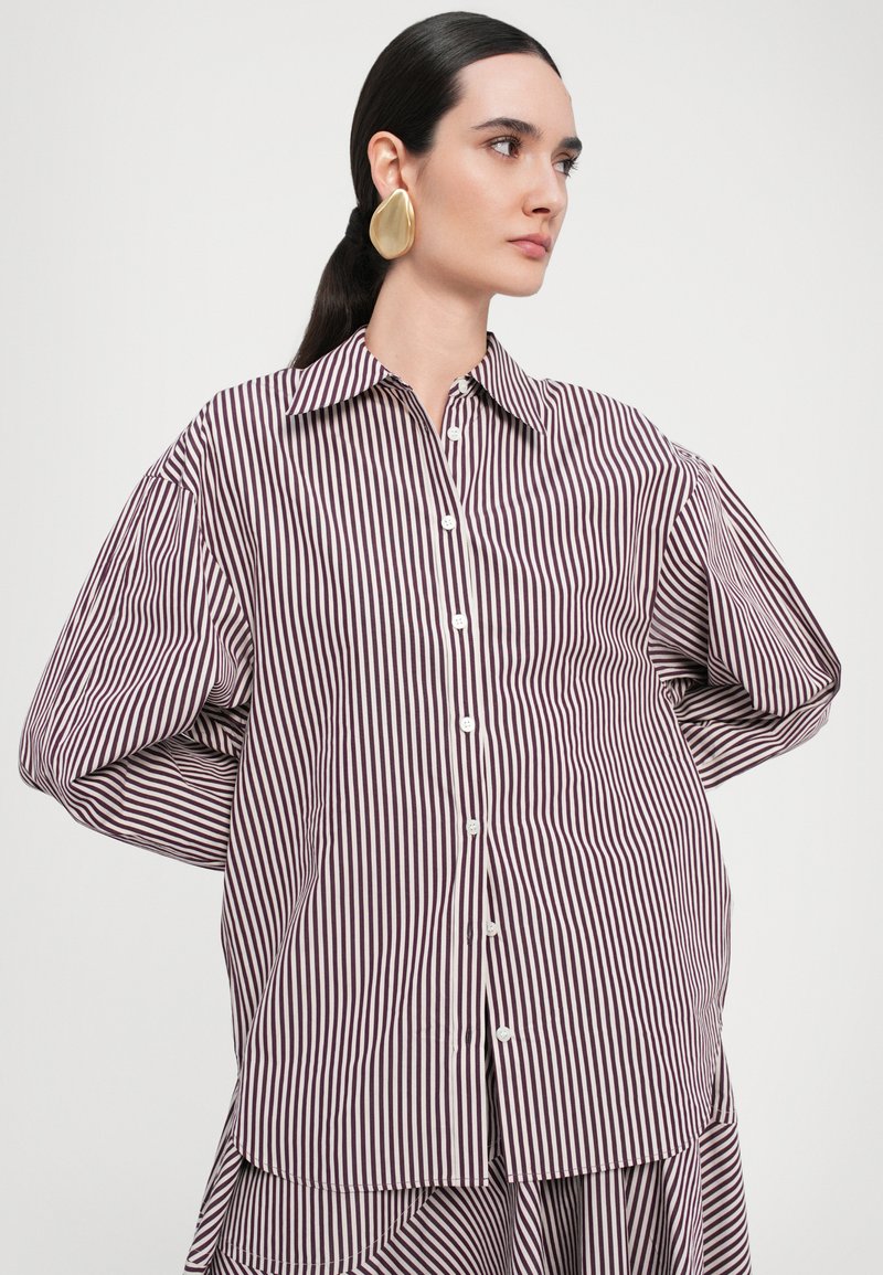 Camicia a righe con pantaloni verticali rossi scuri e bianchi, colletto classico e maniche oversize con una texture morbida.