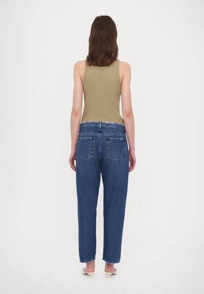 Denim jeans in blue with a relaxed fit, featuring two back pockets and a subtle faded texture, paired with a beige tank top.