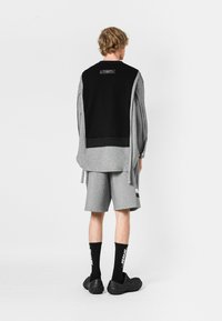 Pantalones cortos grises y una sudadera en capas gris y negra con mangas largas. Calzado negro y calcetas altas negras con texto blanco.