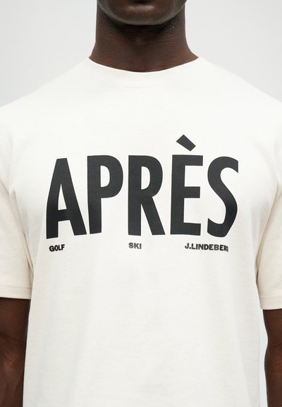 T-shirt de algodão branco com grande texto preto: "APRÈS GOLF SKI J.LINDEBERG." Com mangas curtas e design de gola redonda.