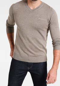 Beige v-ringad tröja i mjukt material med ribbade ärmslut och nederkant; kombinerad med mörka jeans för en avslappnad stil.