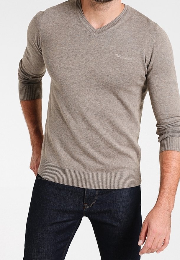 Beige v-ringad tröja i mjukt material med ribbade ärmslut och nederkant; kombinerad med mörka jeans för en avslappnad stil.