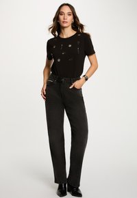 Sort T-shirt med dekorative detaljer, kombineret med højtaljede, lige sorte jeans. Outfittet er akkompangneret af ringe og et armbånd.