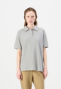 Grå bomullspolo med krage, korte ermer og logo på brystet. Jevn tekstur og avslappet passform, sammen med beige bukser.