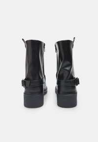 Stivaletti neri in pelle con una superficie liscia, chiusura con zip e un dettaglio con fibbia sul lato. Suola in gomma piatta, design a punta tonda.