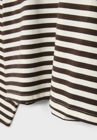 Nahaufnahme eines braun-weiß horizontal gestreiften Stoffs mit sichtbaren Nähten entlang der Saumkanten.