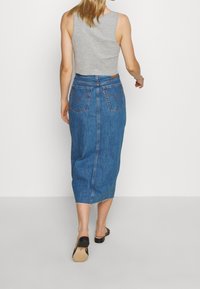 Dżinsowa spódnica w średnim odcieniu niebieskiego, o prostym kroju, do kolan, z postrzępionym dołem i dwoma tylnymi kieszeniami. Połączona z szarym, bezrękawnym topem.