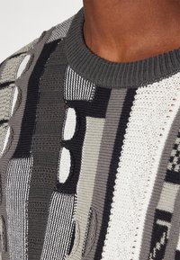 Gebreide trui met een mix van gestructureerde grijze, zwarte en witte patronen met verschillende vormen en een geribbelde ronde hals.