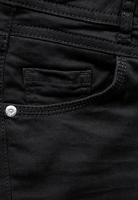 Jeans de mezclilla negra con un pequeño bolsillo frontal, herrajes plateados y costuras en contraste. Textura suave con un diseño ajustado.