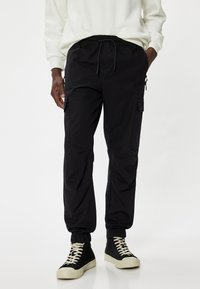 Schwarze Cargo-Hosen mit elastischem Bund, seitlichen Taschen und elastischen Bündchen. Hergestellt aus leichtem Stoff mit glatter Textur.