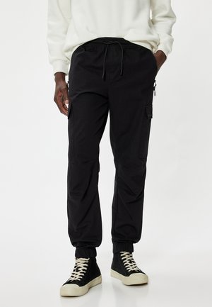 Schwarze Cargo-Hosen mit elastischem Bund, seitlichen Taschen und elastischen Bündchen. Hergestellt aus leichtem Stoff mit glatter Textur.