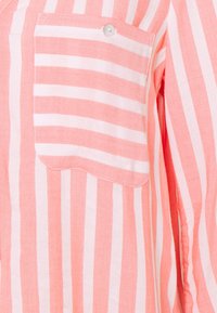 Chemise rayée en tissu rose pâle et blanc, dotée d'une poche à rabat et d'un bouton. Le design présente des rayures verticales avec une finition texturée.