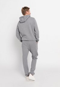 Harmaa huppari ja siihen sopivat jogginghousut, valmistettu pehmeästä kankaasta, jossa on normaali istuvuus ja elastiset hihansuut, yhdistettynä valkoisiin lenkkareihin.