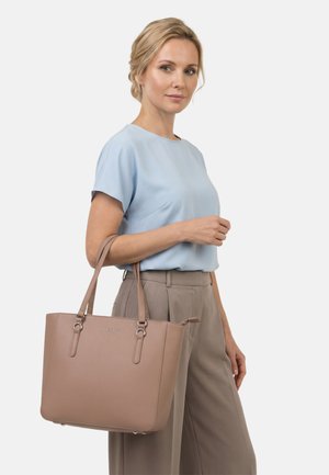 Nő világoskék blúzban és taupe színű nadrágban, kezében egy nagy taupe bőr kézitáskával, dupla pánttal.