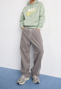 Ljusgrön hoodie med "Nike"-logotyp; grå bredbenta byxor i kordflers; mönstrad textur; i kombination med grå och teal-sneakers.